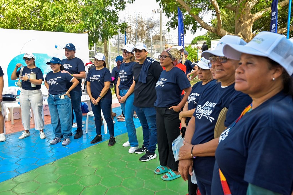 Grupo numeroso de voluntarios con camisetas azules "Juntos por el Progreso" reunidos frente a un pendón institucional de Surtigas en el barrio Torices.