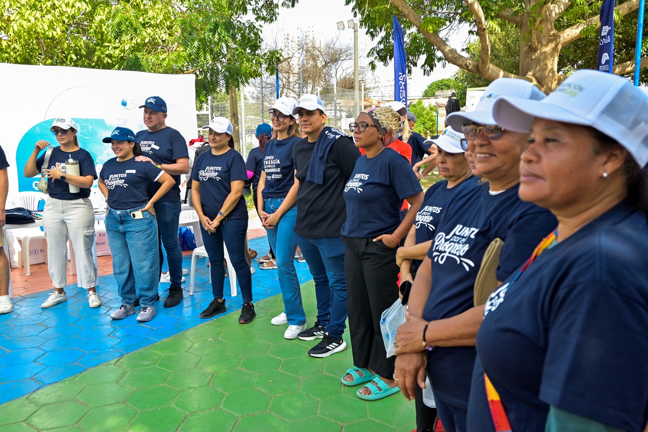 Grupo numeroso de voluntarios con camisetas azules "Juntos por el Progreso" reunidos frente a un pendón institucional de Surtigas en el barrio Torices.
