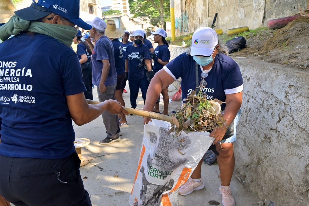 Voluntarios con gorras de Fundación Promigas recogen maleza en bolsas durante una jornada de limpieza comunitaria en Torices, Cartagena.